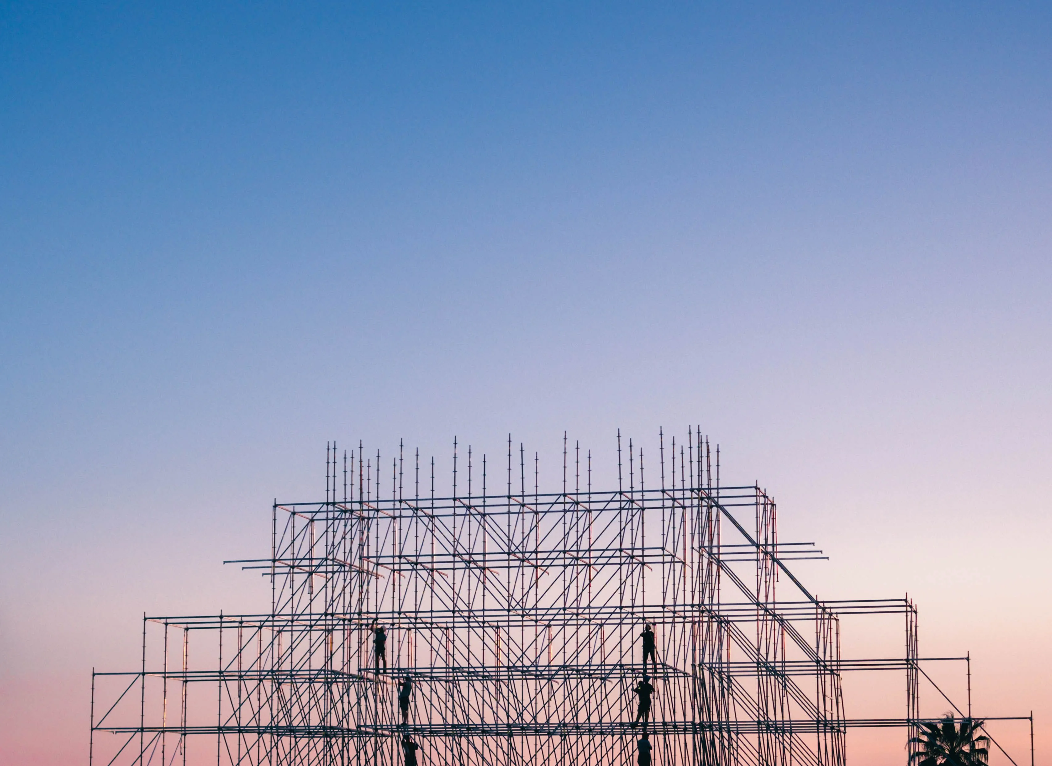 Construction professionals working on a large scaffold structure at dusk